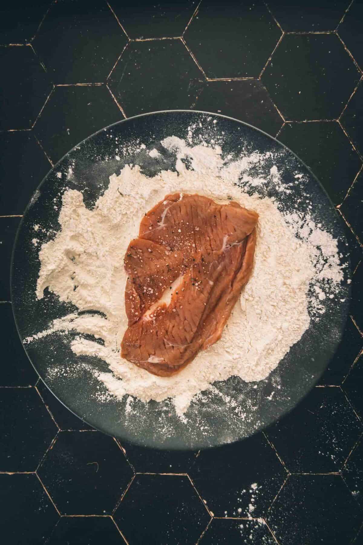 Um pedaço de vitela num prato com farinha.