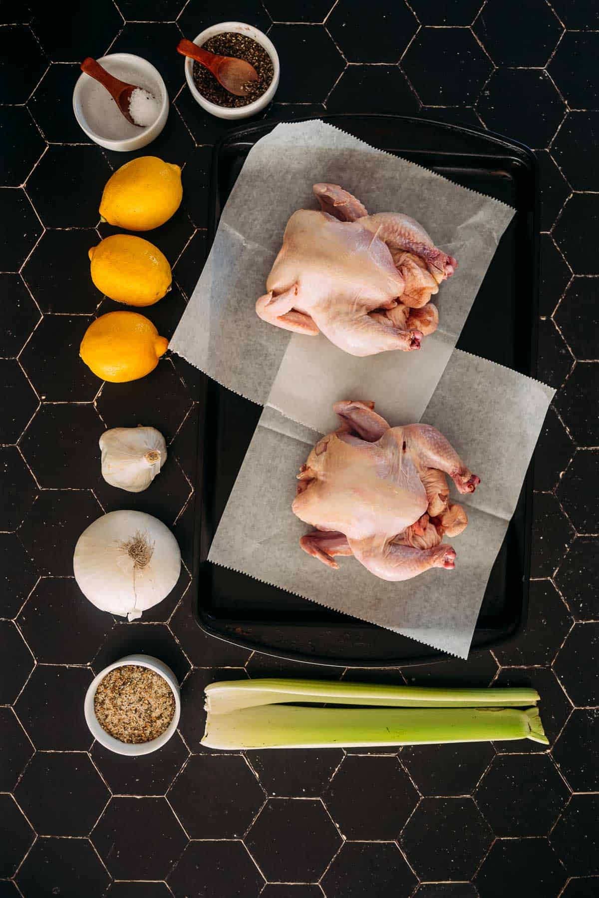 Ingredientes incluindo galinhas de caça, limão e aipo em uma mesa para a receita.
