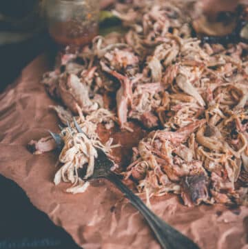 carne de porco desfiada em papel pardo com garfo e molho ao fundo.