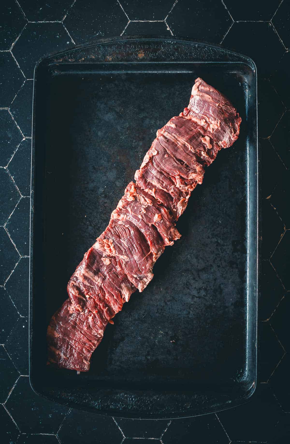 Um bife cru fica em uma assadeira preta para mostrar a textura única do corte.