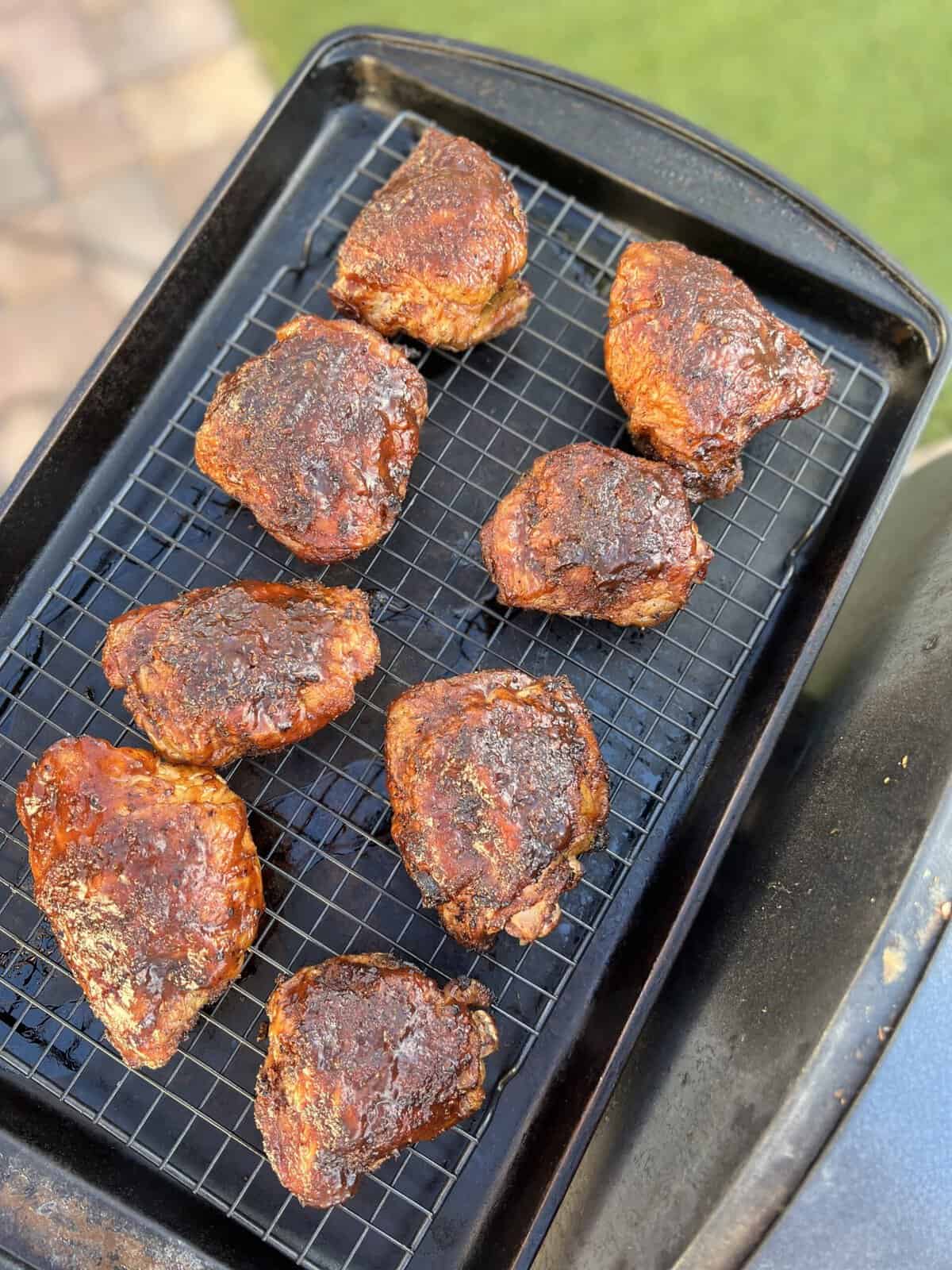 Coxas de frango defumado em uma assadeira ao lado da grelha.