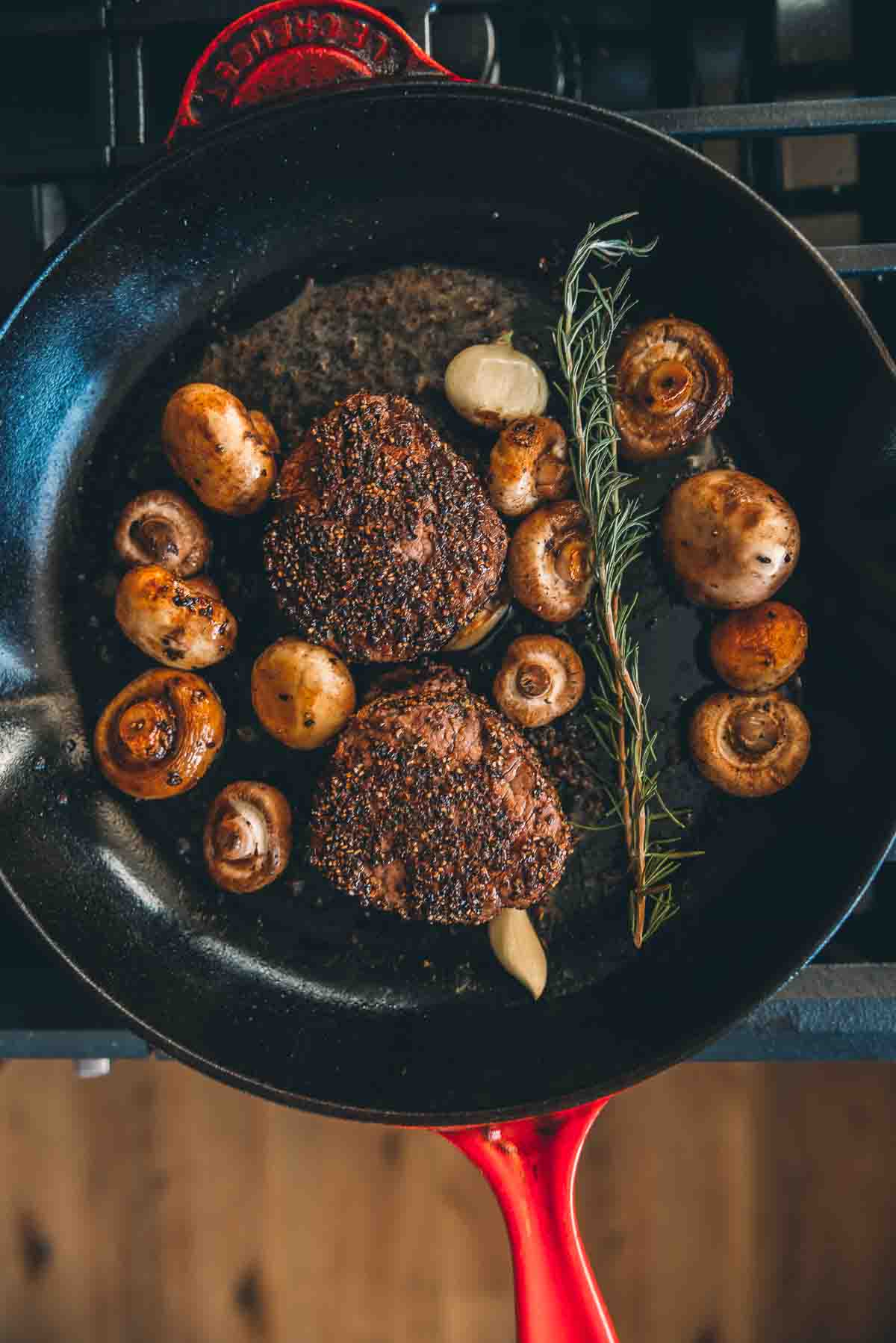 Filetes grelhados numa frigideira com cogumelos, manteiga, alecrim e alho. 