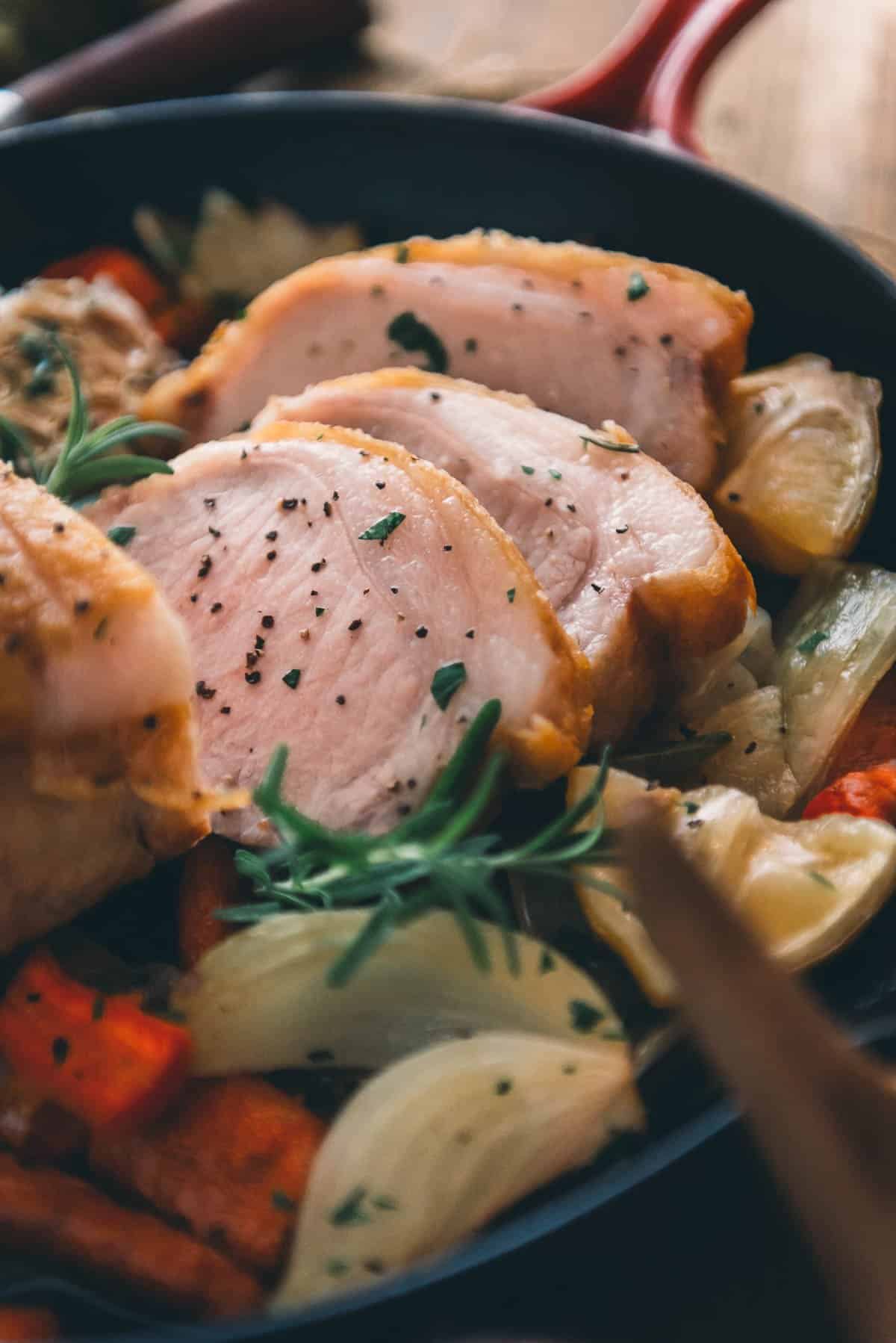 Uma frigideira de ferro fundido cheia de fatias de porco e legumes sobre uma mesa.