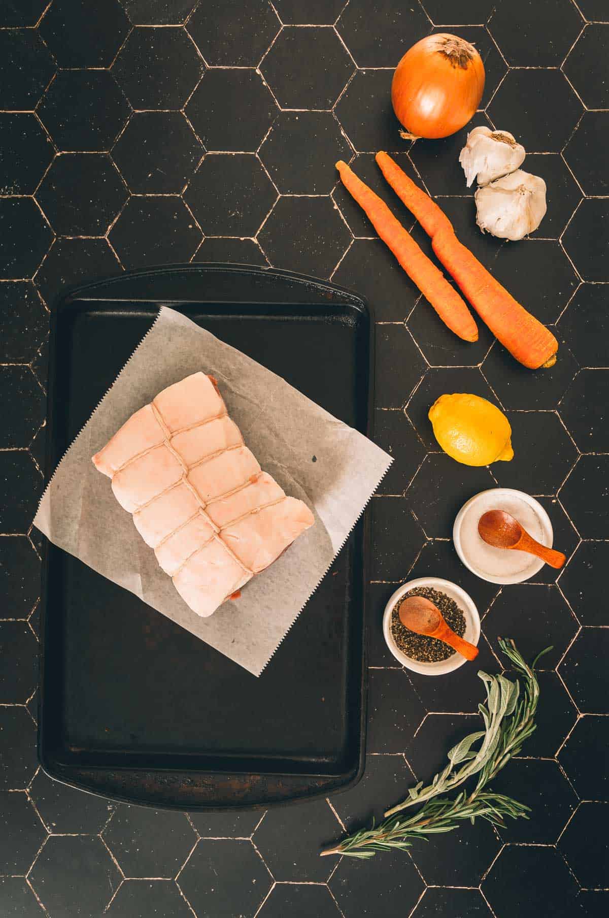 Uma bandeja com lombo de porco, cenouras e especiarias e outros ingredientes.