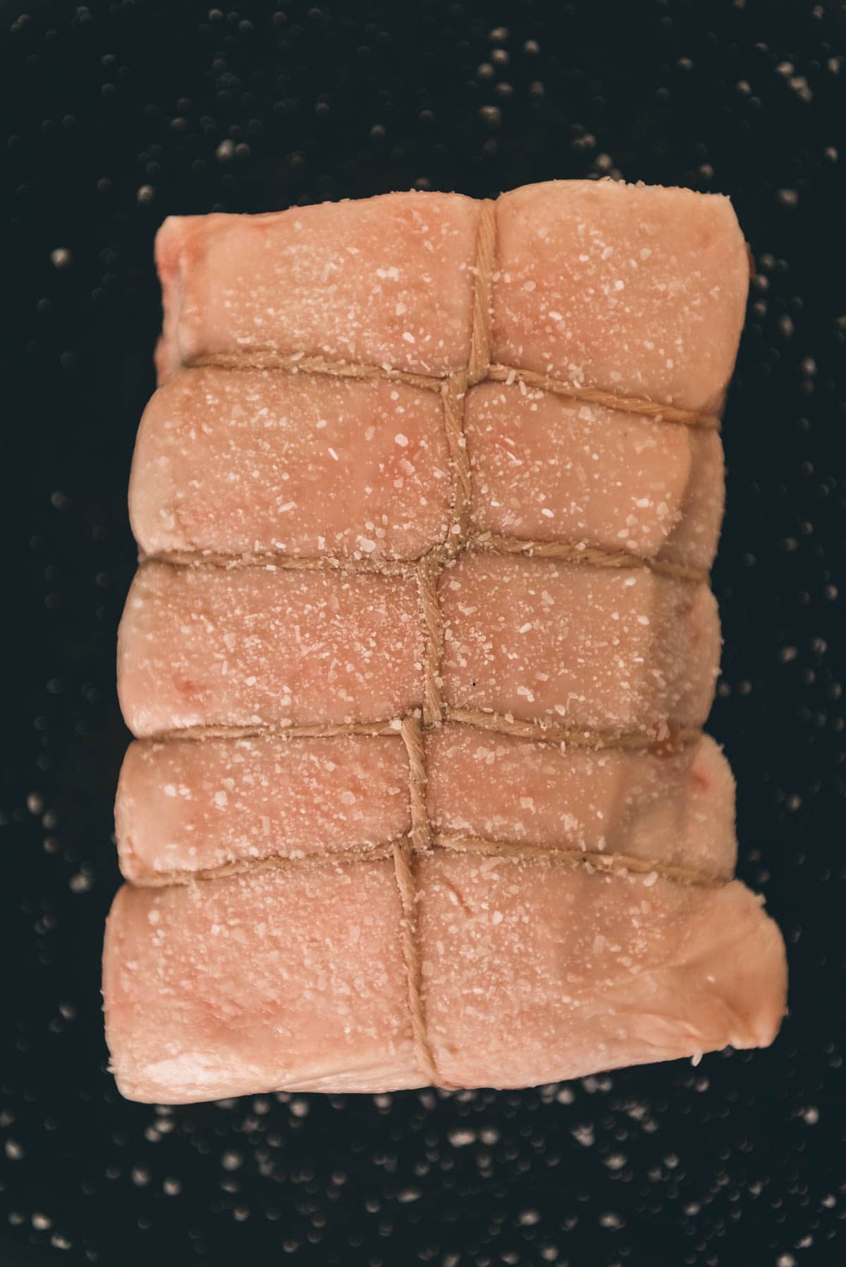 Um close de um pedaço de carne de porco que foi salgado em uma superfície preta.