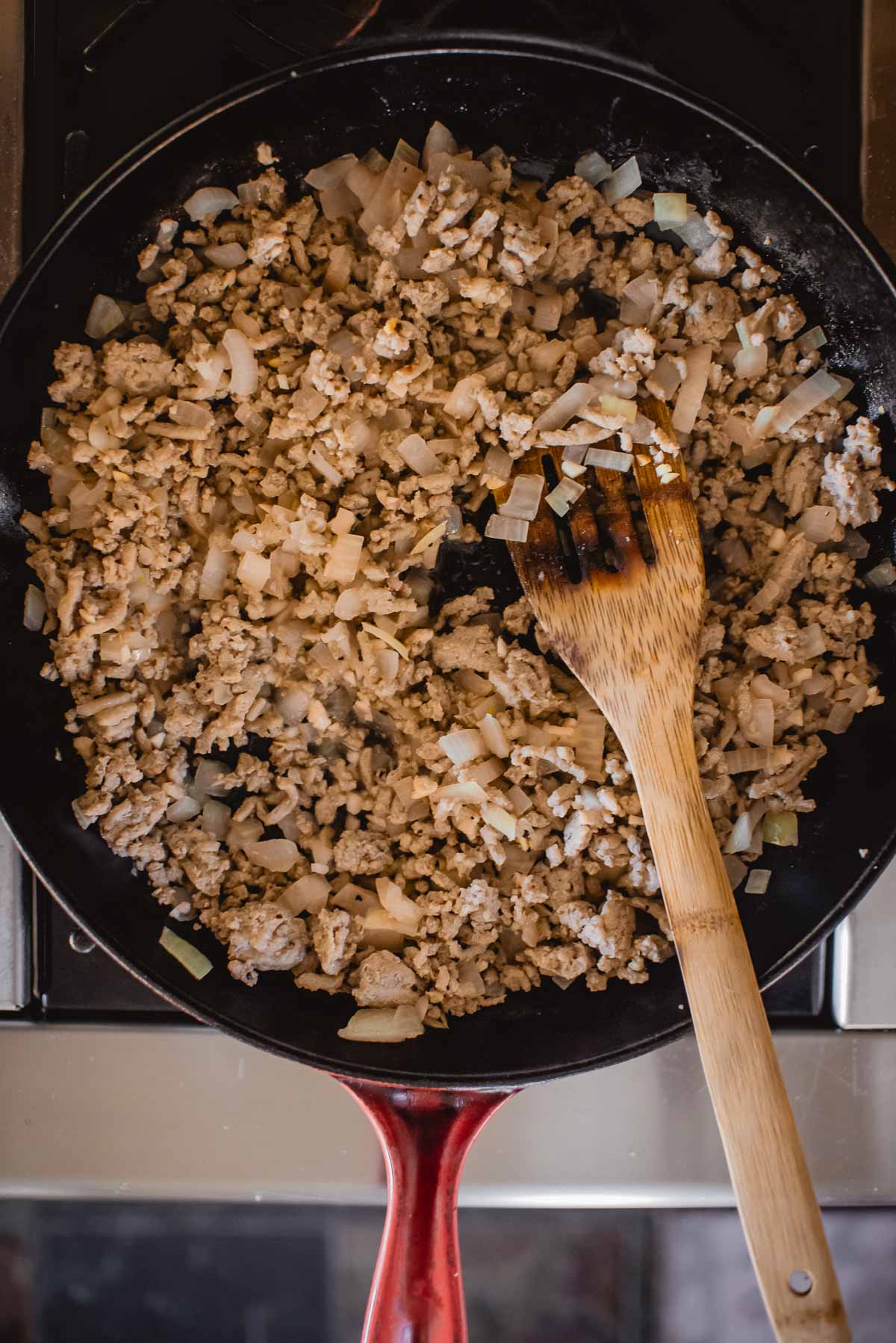 Peru moído e cebola picada cozinhando em uma panela de cabo vermelho com uma espátula de madeira.