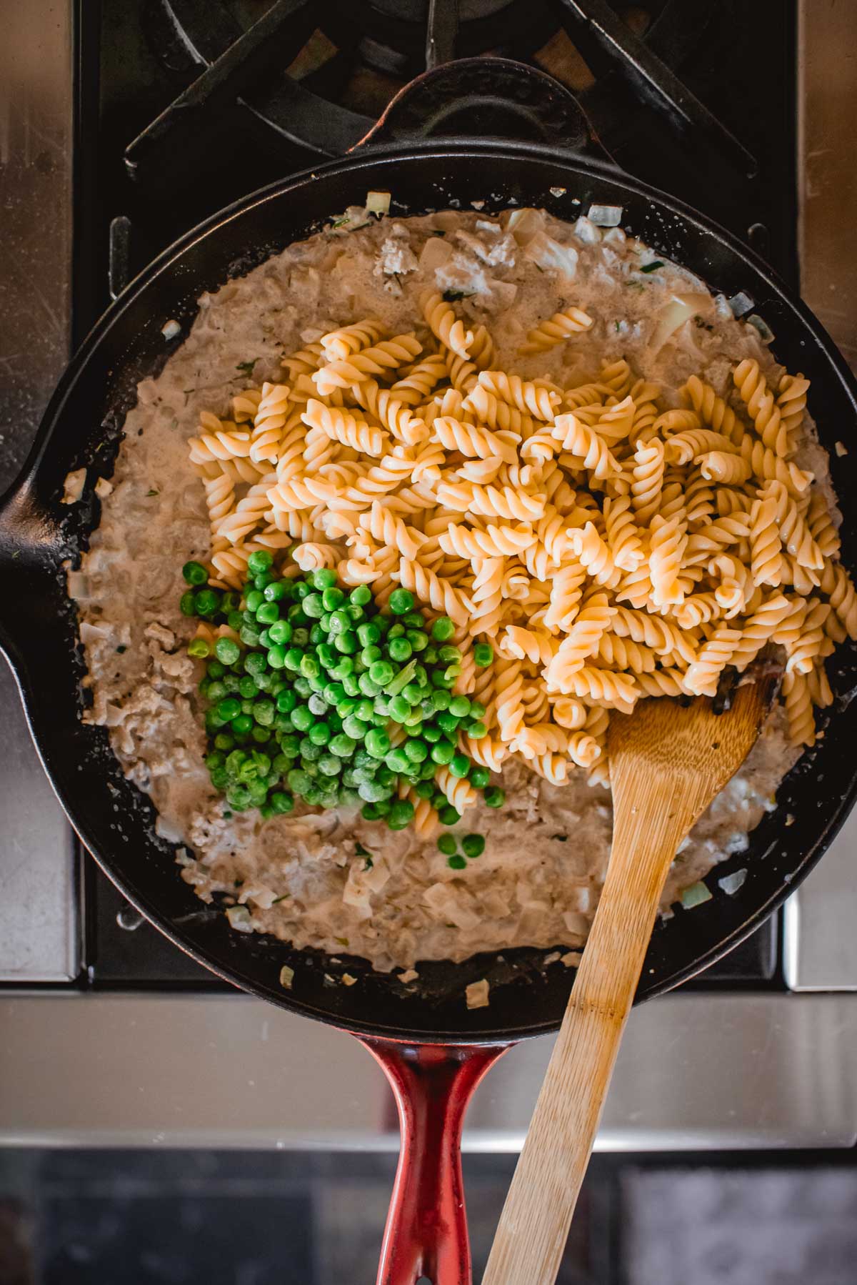 Uma frigideira com molho cremoso, macarrão, peru moído e ervilhas, com uma colher de pau no fogão.