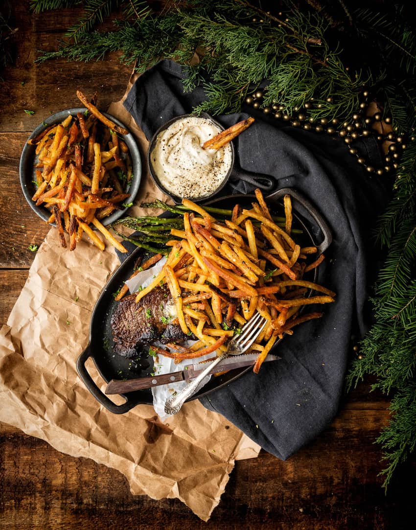 Uma dose escura e temperamental de filé com batatas fritas com uma pilha de batatas fritas ao lado.