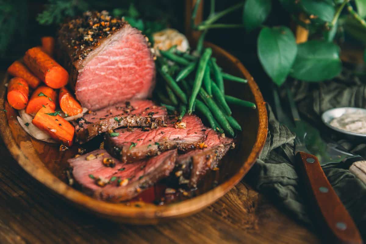 Um prato de carne, cenoura e feijão verde sobre uma mesa de madeira.