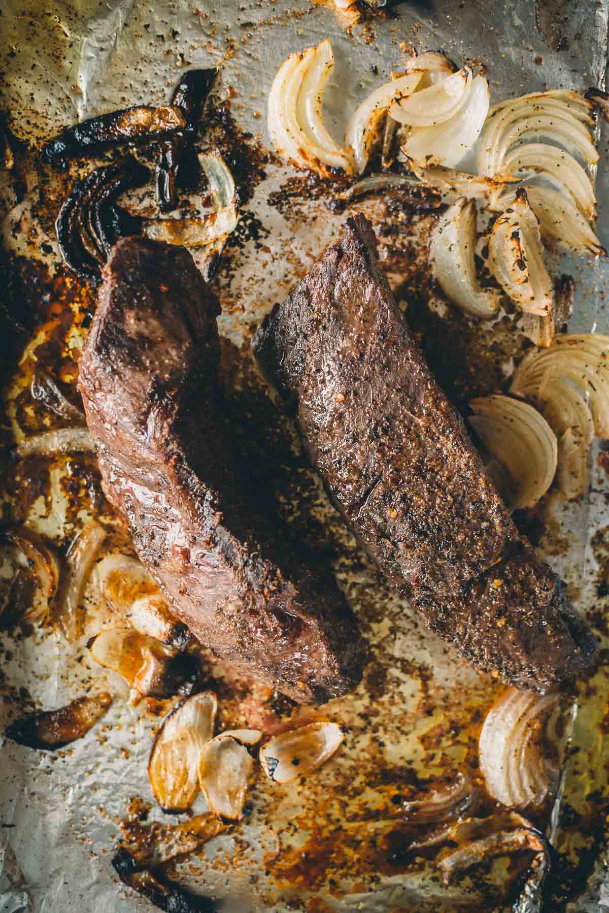 Dois bifes grelhados em uma assadeira com rodelas de cebola assada.