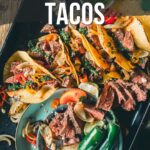 Uma frigideira recheada com tacos de bife grelhado, guarnecido com cebolas fatiadas, jalapeños e ervas.