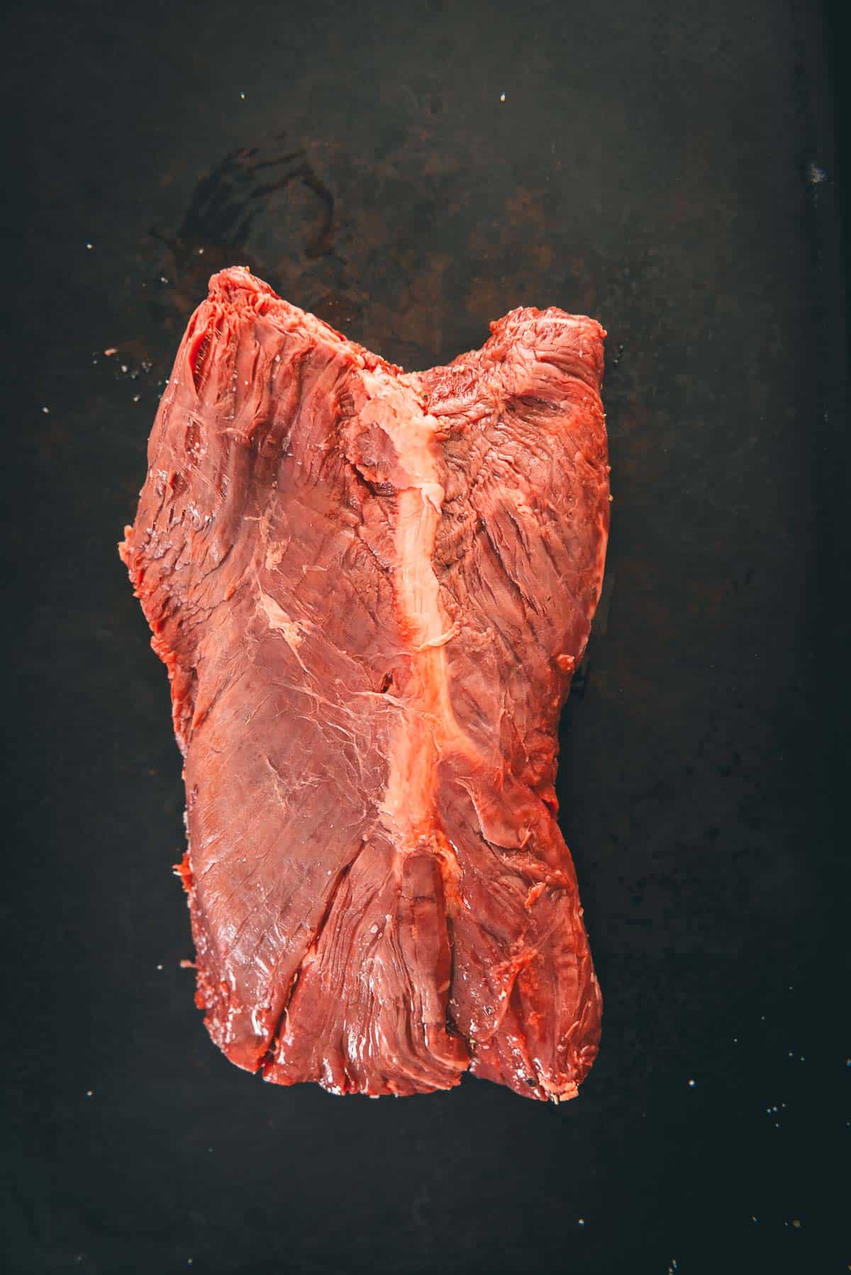 Um pedaço de bife em uma frigideira preta, mostrando o tecido conjuntivo característico no centro.