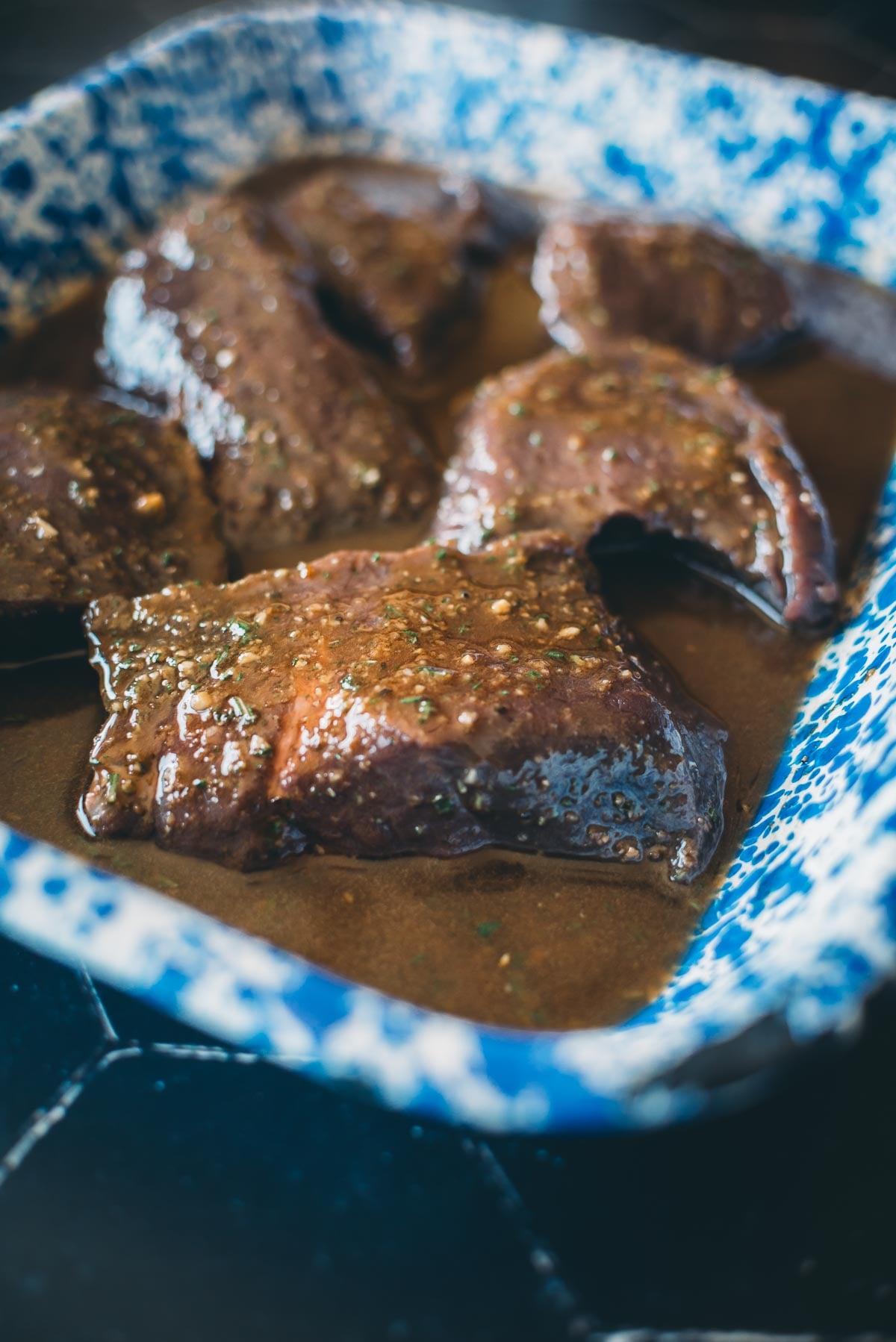 Fatias de carne em molho marrom espesso, servidas em prato salpicado de azul e branco.