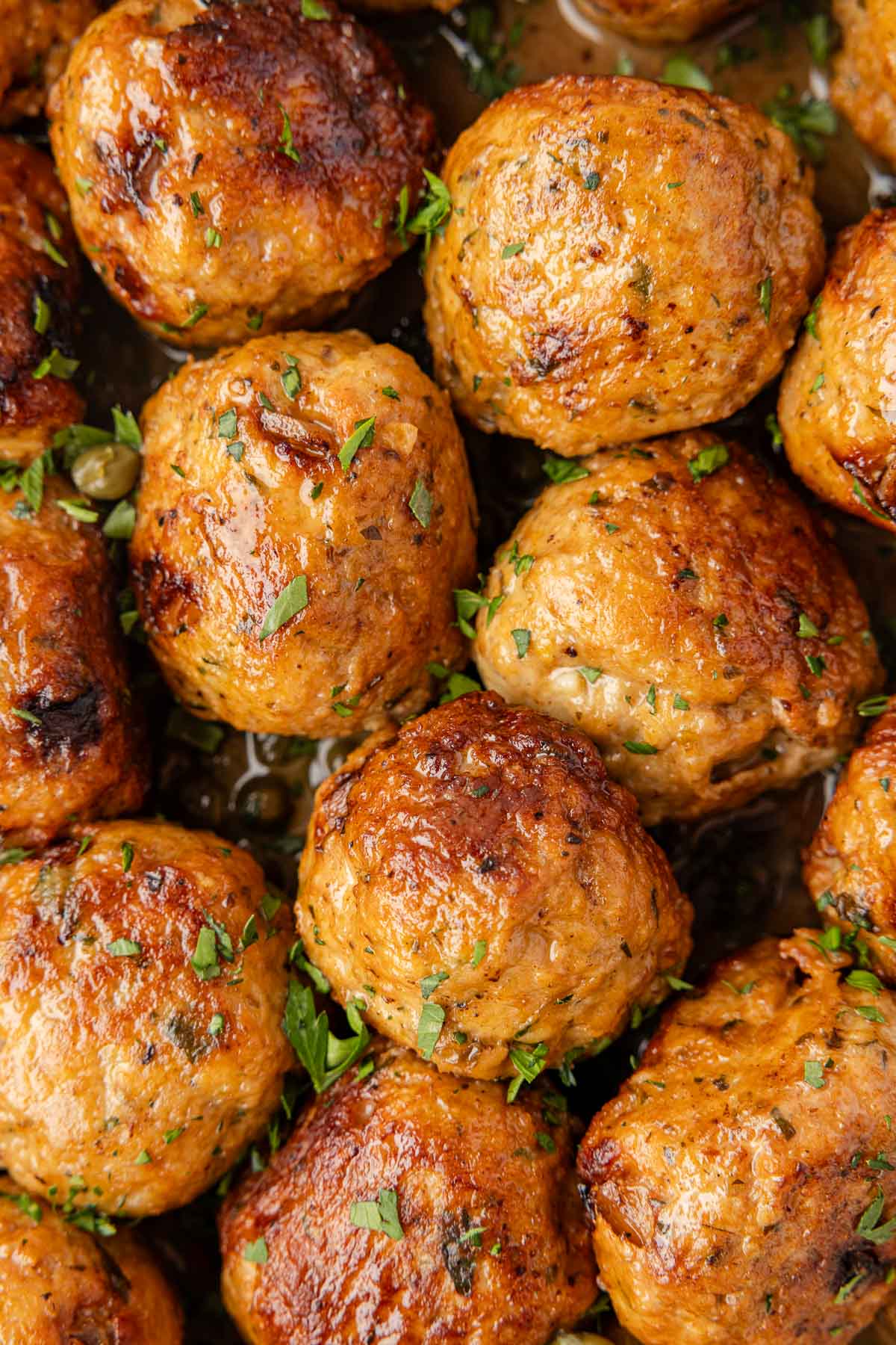 Close-up de várias almôndegas de frango Piccata douradas, decoradas com ervas picadas.