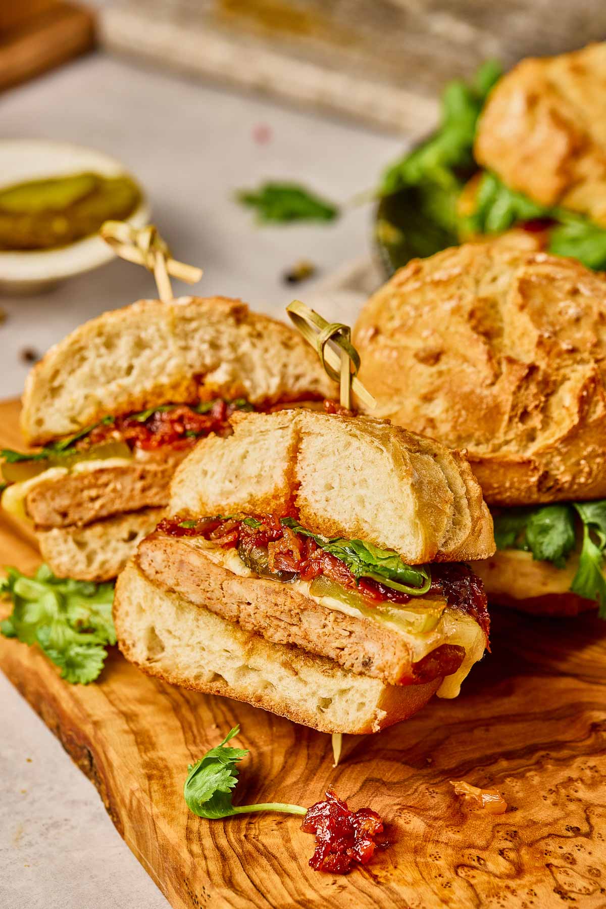 Hambúrguer de frango Gochujang com hambúrguer de frango, queijo, verduras e geléia de bacon kimchi, cortado ao meio e servido em tábua de madeira com guarnição de coentro.