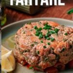 Um prato de tártaro de salmão decorado com cebolinhas picadas e servido com rodelas de limão. O texto diz: "Como fazer tártaro de salmão. Obtenha a receita completa em girlcarnivore.com.