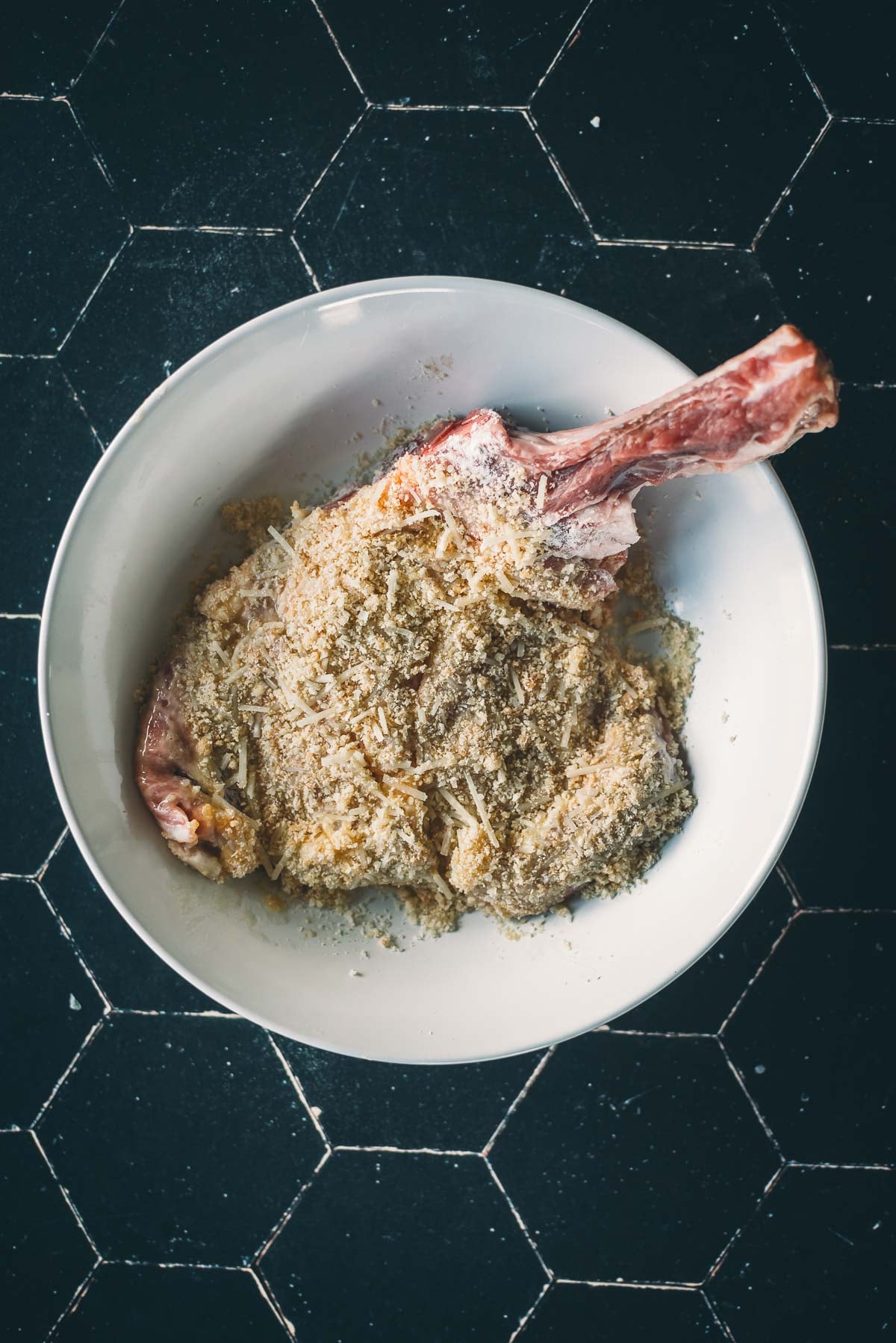 Uma costeleta de vitela crua com osso em uma tigela branca para ser revestida com empanado.