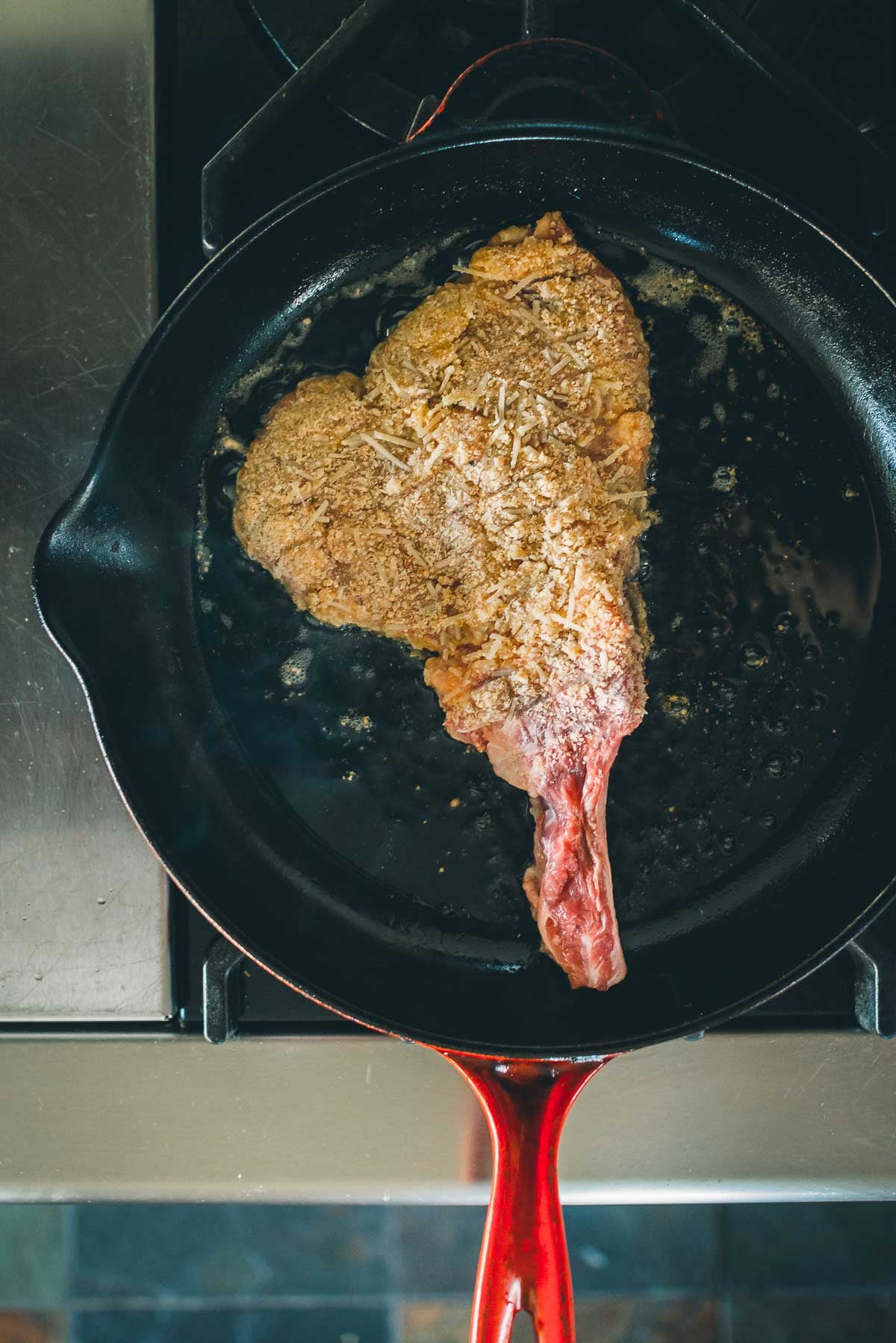 Uma costeleta de vitela à milanesa está sendo cozida em uma frigideira de ferro fundido no fogão.