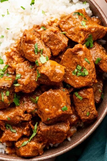 Um close de vindaloo de cordeiro com molho vermelho e coentro picado servido com arroz branco em uma tigela.