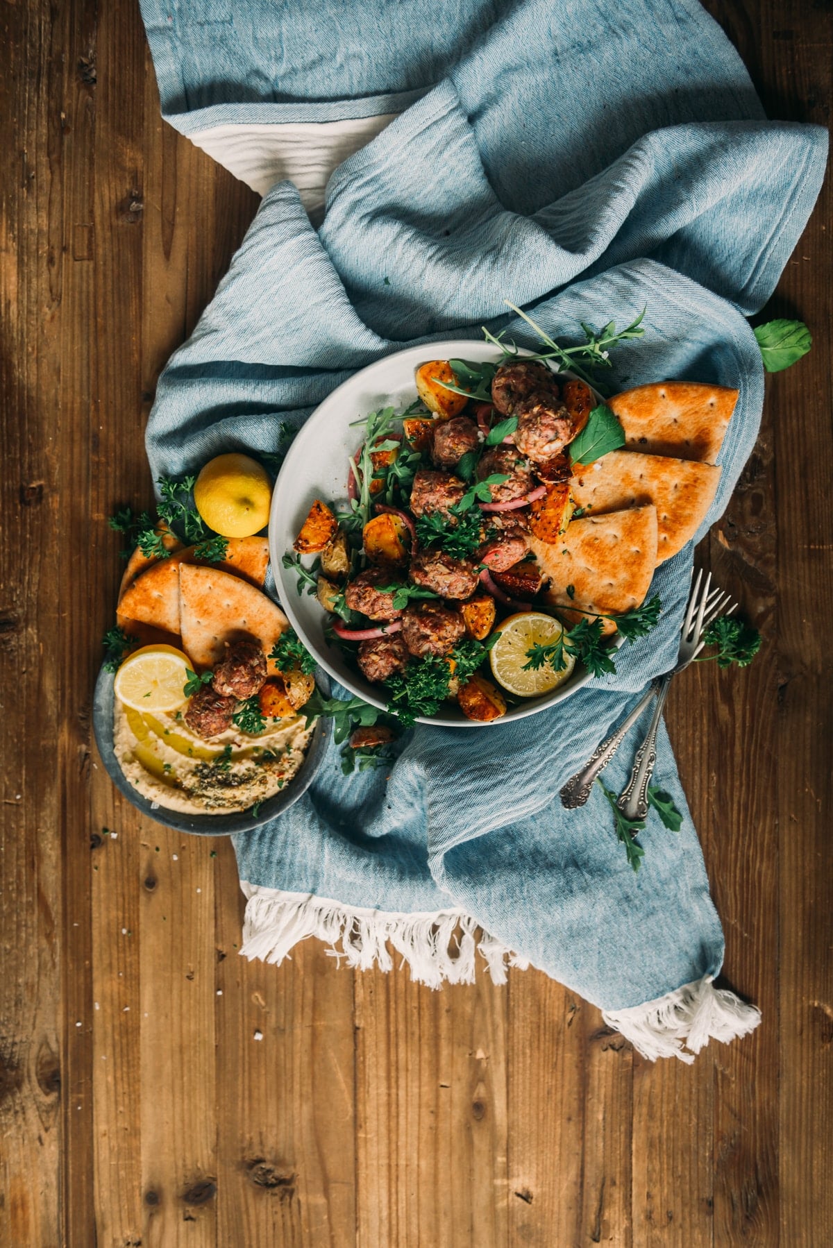 foto acima de uma tigela recheada com almôndegas de cordeiro, decorada com ervas frescas e limão, servida com batatas assadas e pão árabe