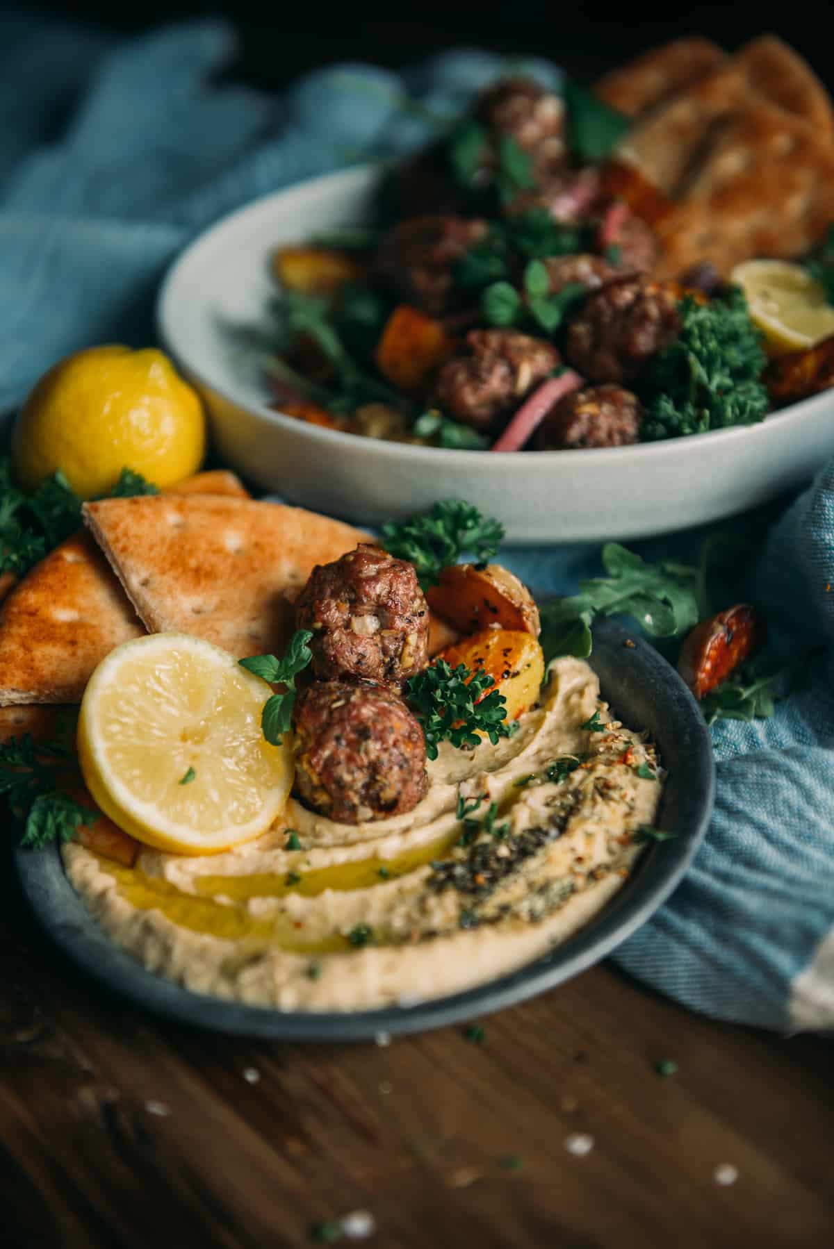 almôndegas de cordeiro com alecrim e dijon em um prato pequeno com hummus, limões e ervas