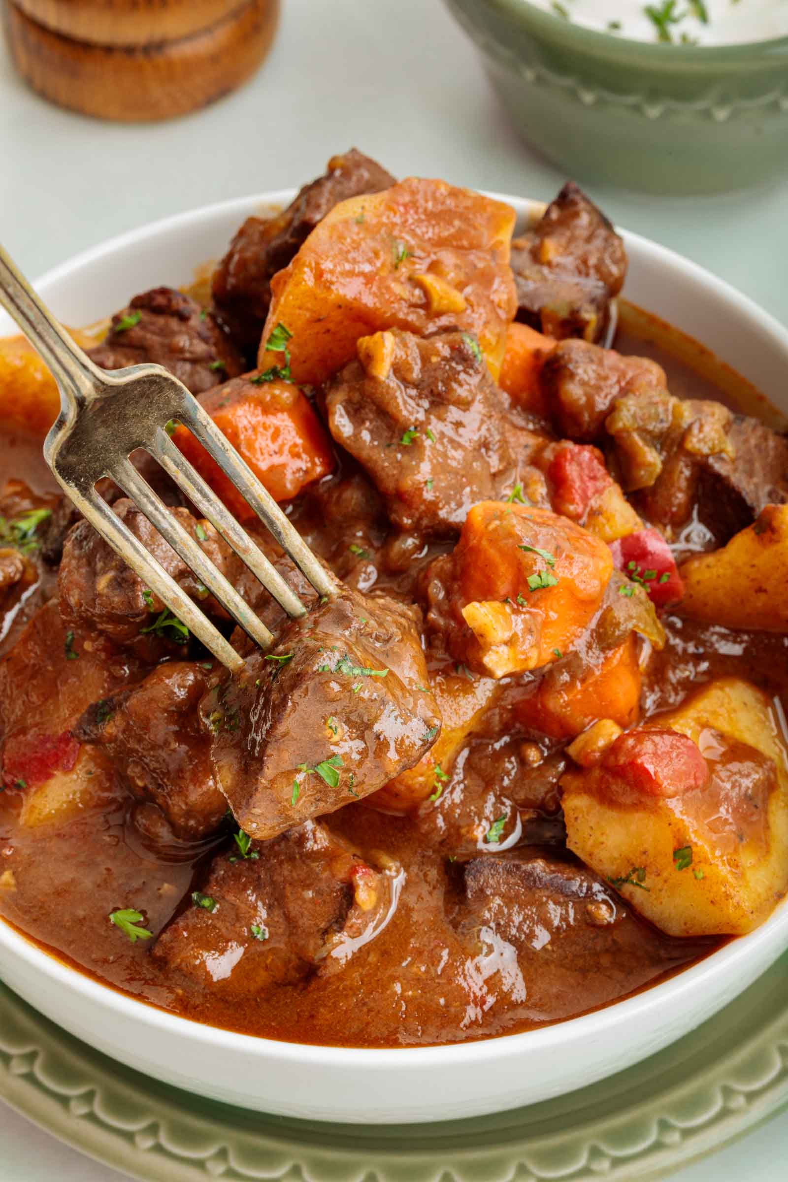 Uma tigela de ensopado de carne com pedaços de coração de boi, batatas e cenouras em molho marrom, com um garfo pegando um pedaço de carne.