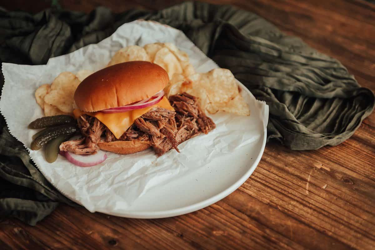Um sanduíche de carne de porco desfiada com batatas fritas num prato branco.