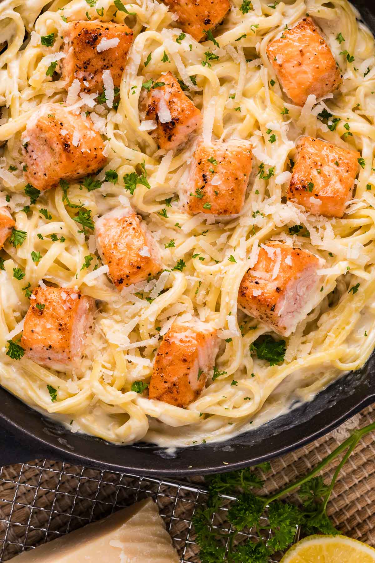 Um close de Alfredo cremoso coberto com pedaços de salmão, queijo ralado e salsa picada em um prato preto.