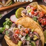 Dois tacos de carne assada cobertos com cebola picada, coentro e molho são servidos em um prato preto com rodelas de limão e rodelas de rabanete.