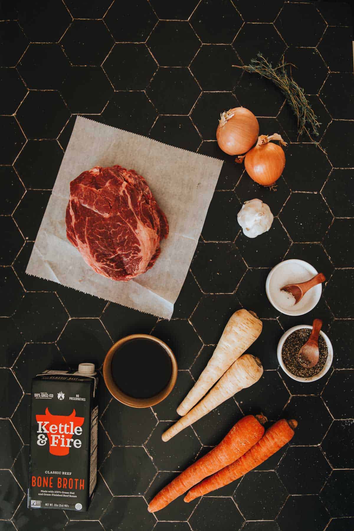 Carne, cenoura, cebola e temperos são colocados sobre a mesa para esta receita.