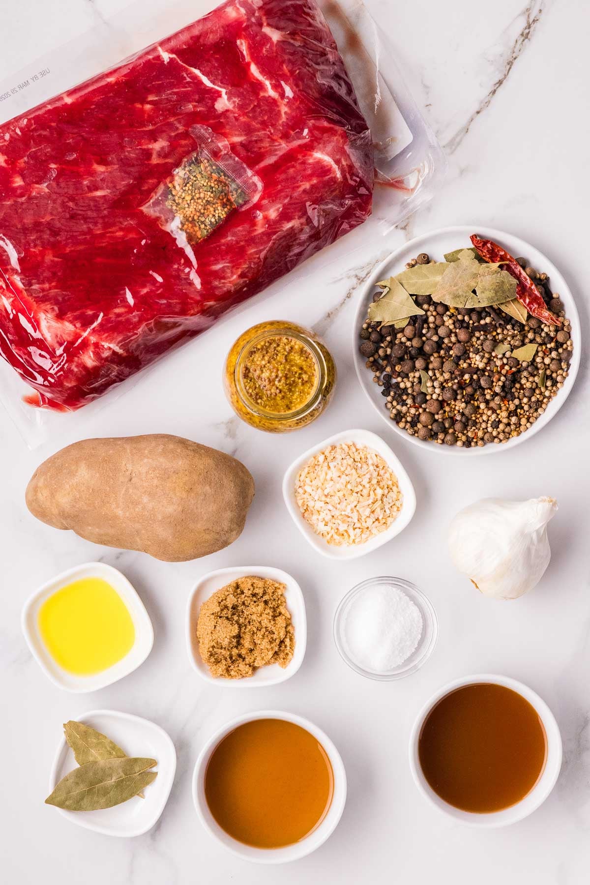 Carne enlatada crua em embalagens, temperos, batata, alho, mostarda, óleo, açúcar mascavo, sal e líquidos dispostos sobre uma superfície de mármore branco.